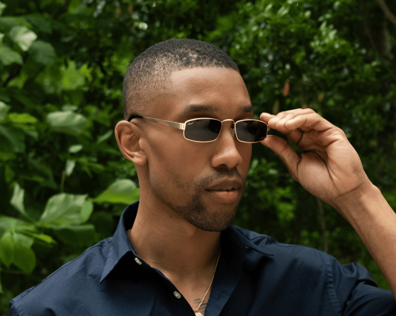 Man wearing Maono sunglasses and a dark blue shirt against a green leafy background